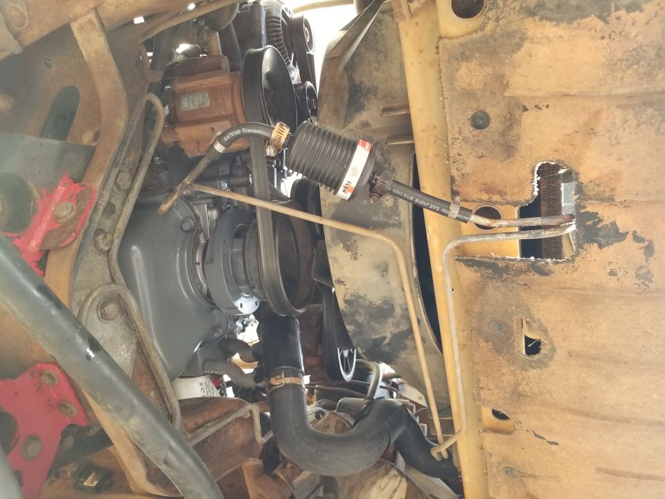 Engine bay of rusty truck frame showing power steering pump, belt, and steering shaft