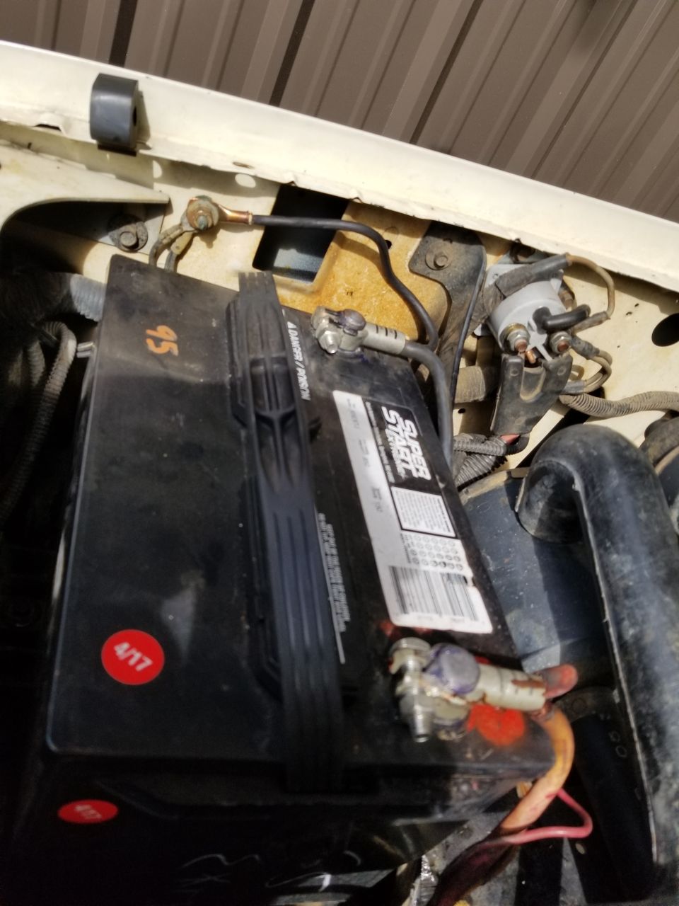 Car battery with red and white label, connected to terminals and wiring