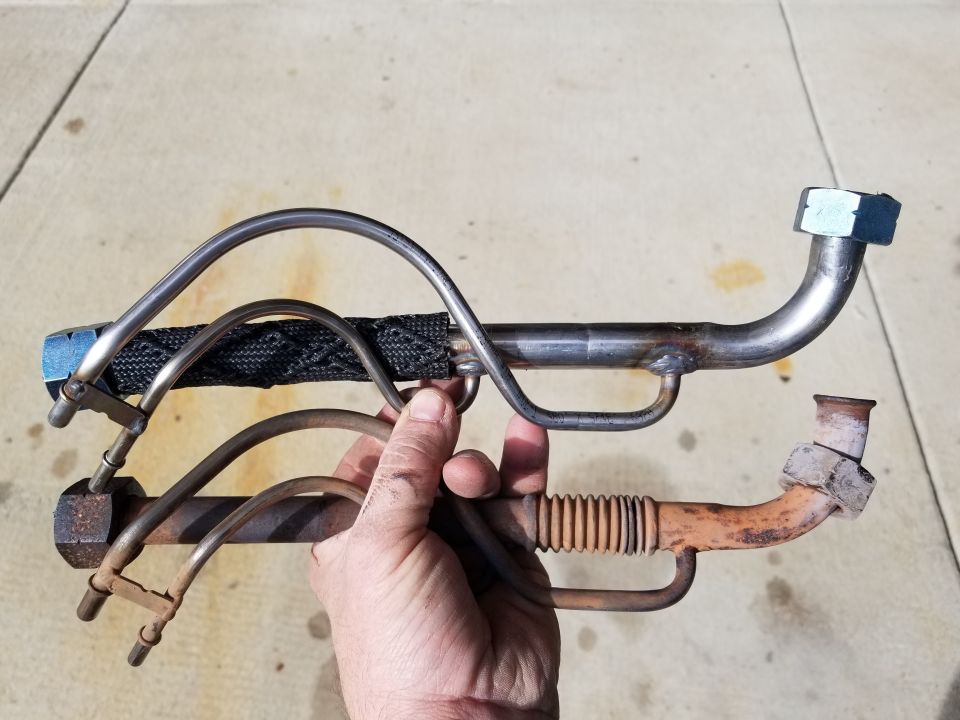 Two metal fuel lines, one with black heat shielding, held by a hand