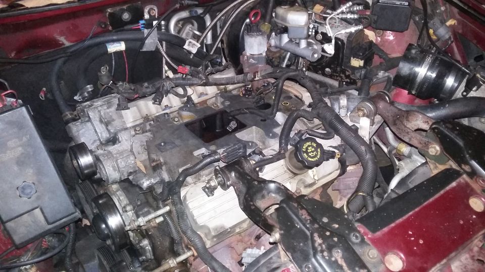 Disassembled engine bay with hoses, wiring, and engine parts visible.