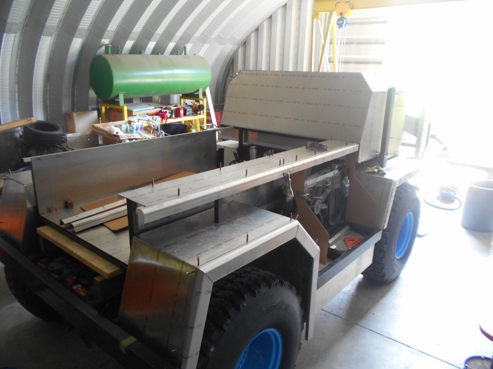 Custom vehicle under construction with metal body, large tires, and blue rims.