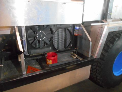1992 Ford Bronco - The front of a custom vehicle build shows a large radiator with two fans, a red bucket, and a large tire with a blue rim on the right side.
