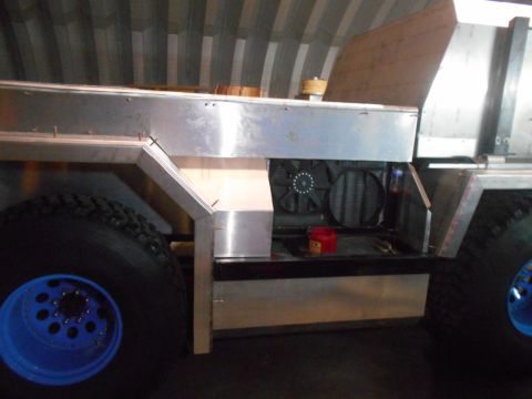 1992 Ford Bronco - The side view of a custom-built vehicle shows a large tire with a blue rim and a section of the aluminum body with exposed engine component…