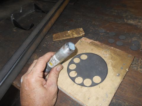 1992 Ford Bronco - A hand holds a threaded metal pipe fitting over a circular piece of black material with several holes cut out of it. Several small circular…
