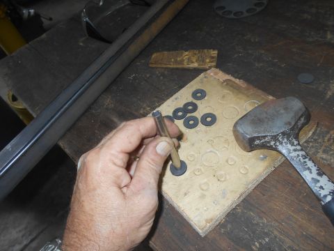 1992 Ford Bronco - A person's hand is holding a metal tube over a wooden block with several circular washers. A hammer rests on the block next to the washers.
