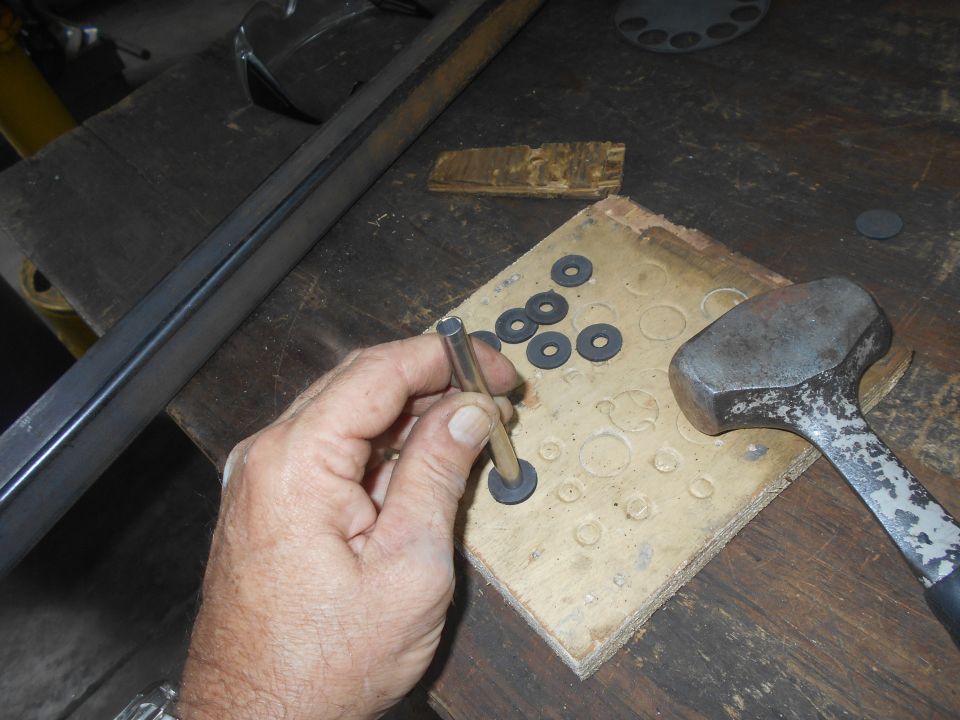 Hand holding metal tube over wooden block with washers and hammer
