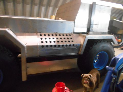 1992 Ford Bronco - A custom-built vehicle with large tires and a metal body is under construction inside a garage. A bulldog stands near the large tire.