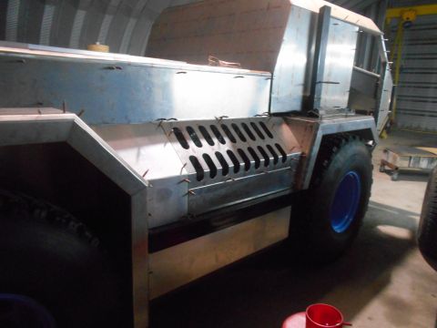 1992 Ford Bronco - A custom-built, unfinished vehicle chassis with large tires and a blue wheel rim is shown in a workshop setting. The vehicle features a met…
