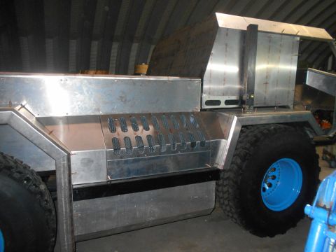 1992 Ford Bronco - A custom-built vehicle with a brushed aluminum body and large off-road tires with bright blue rims is shown in a workshop setting. The vehi…