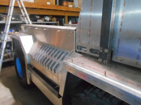 1992 Ford Bronco - The side of a custom-built aluminum vehicle with a large tire and blue wheel is shown in a workshop setting. Vented panels are visible on t…