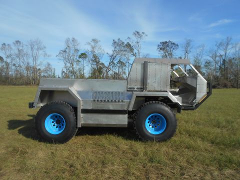 1992 Ford Bronco - A custom-built, four-wheeled vehicle with a brushed aluminum body and bright blue rims is parked in a grassy field with trees in the backgr…