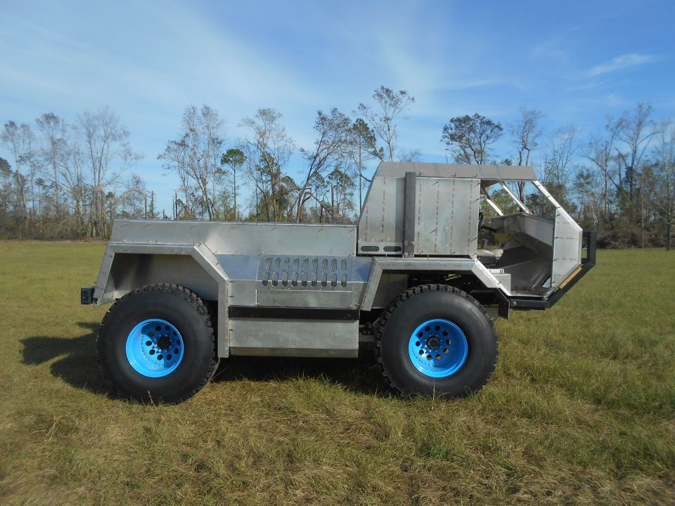 Custom four-wheeled vehicle with aluminum body and blue rims in a grassy field.