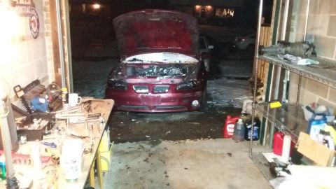 Dark red Pontiac Grand Prix with hood open in a snowy garage, engine exposed, tools and fluids nearby.