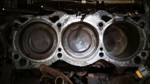 Overhead view of V6 engine cylinders and pistons, showing wear and carbon buildup.
