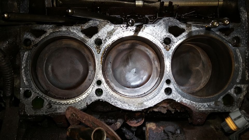 Overhead view of V6 engine cylinders and pistons, showing wear and carbon buildup.