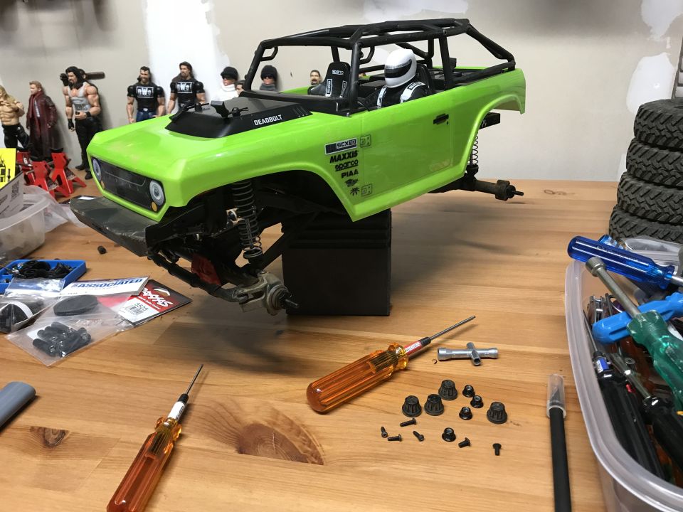 Green RC car body on chassis with tools and parts on a wooden workbench.