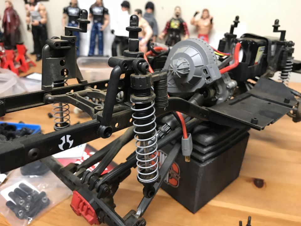 Remote controlled car chassis and suspension with action figures in the background.
