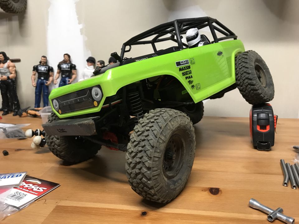Green RC rock crawler truck with action figures in the background.