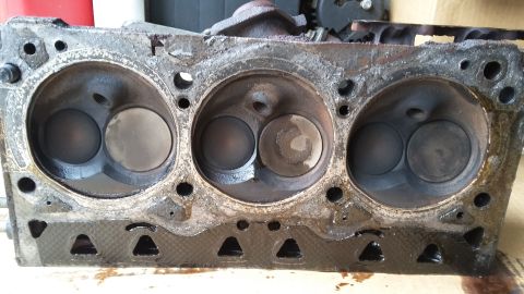 Used engine cylinder head with three combustion chambers, showing heavy oil and carbon buildup.
