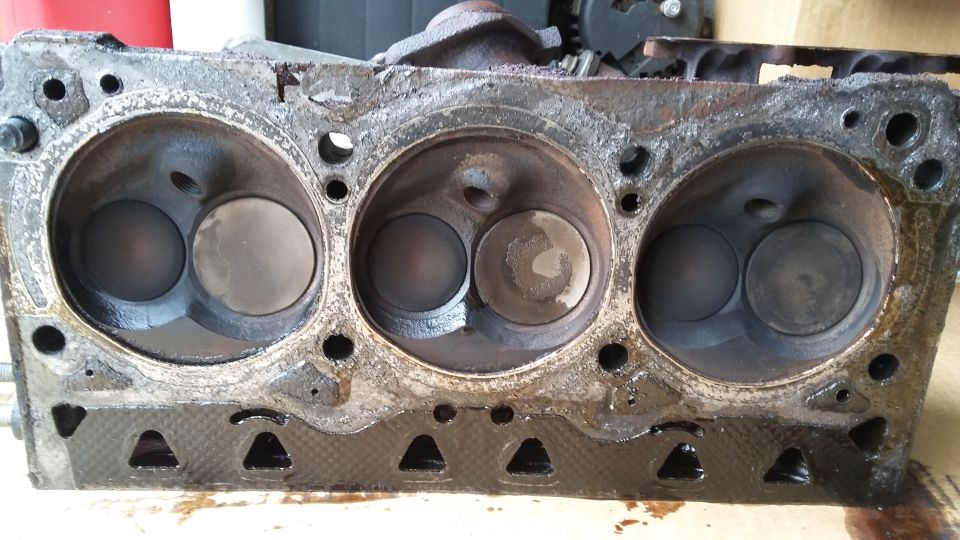 Used engine cylinder head with three combustion chambers, showing heavy oil and carbon buildup.