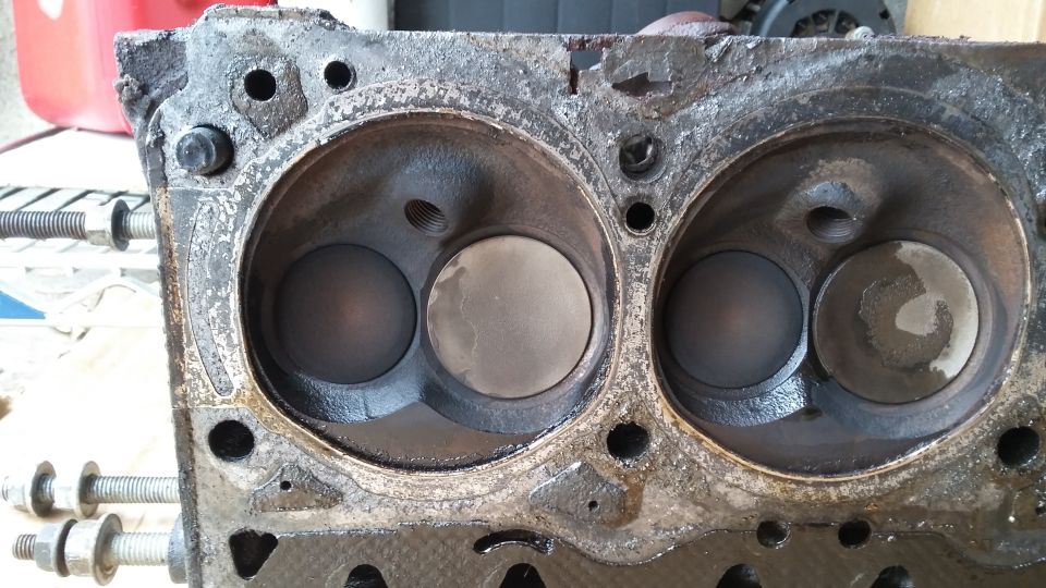 Engine cylinder head with two combustion chambers showing carbon buildup and valve wear.