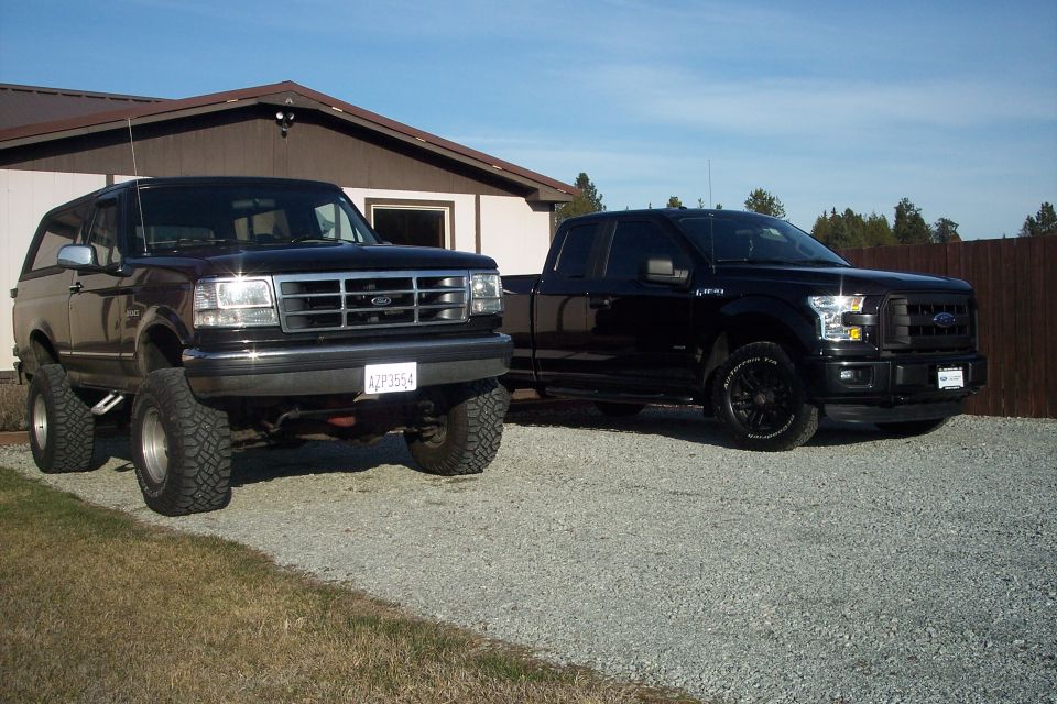 Two black Ford trucks parked on a gravel driveway.