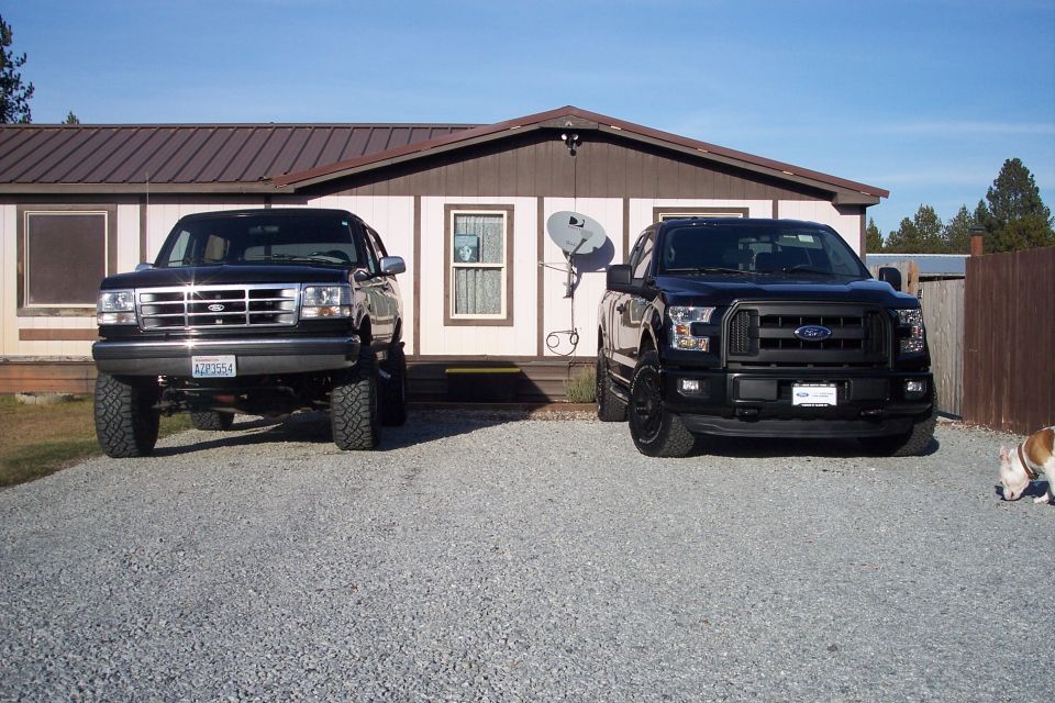 Two black Ford pickup trucks parked in front of a house.