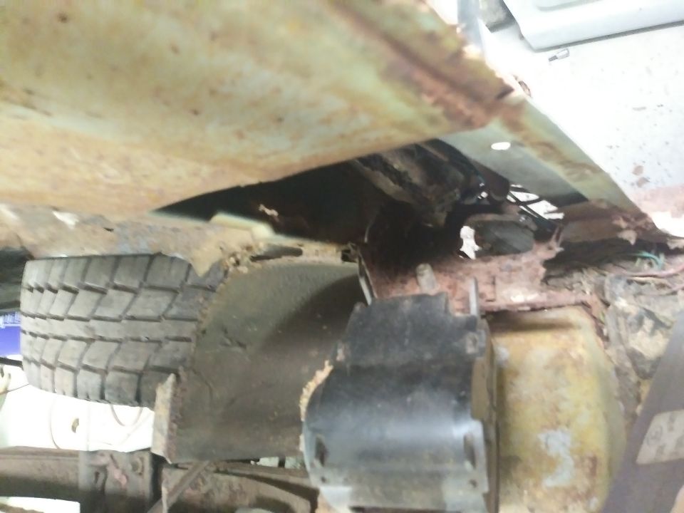 Underside of a rusty vehicle showing tire, suspension, and wiring