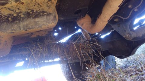 1996 Ford Bronco - The underside of a vehicle shows a large accumulation of dry grass and straw packed between the frame and exhaust system. The vehicle appea…