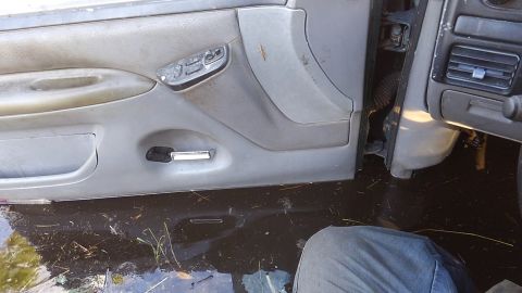 1996 Ford Bronco - The interior of a vehicle shows a flooded driver's side door panel and dashboard. Water, debris, and grass are visible on the floor of the…