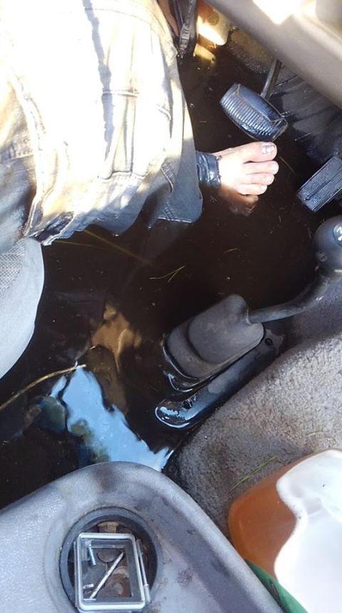 1996 Ford Bronco - The interior of a vehicle is flooded with dark water. A bare foot is visible near the pedals, and a person's legs in jeans are also submerg…