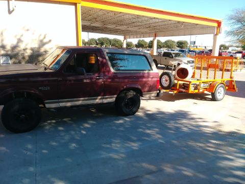 1996 Ford Bronco - A maroon 1990s Ford Bronco is parked next to an orange utility trailer loaded with a concrete mixer. The vehicle and trailer are parked und…