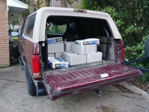 1996 Ford Bronco - The open tailgate of a dark red Ford Bronco reveals the cargo area filled with bags of mortar mix and concrete blocks. The vehicle is parke…