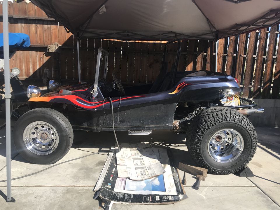 Custom dune buggy with flame decals, parked under a canopy. Front and rear wheels are visible