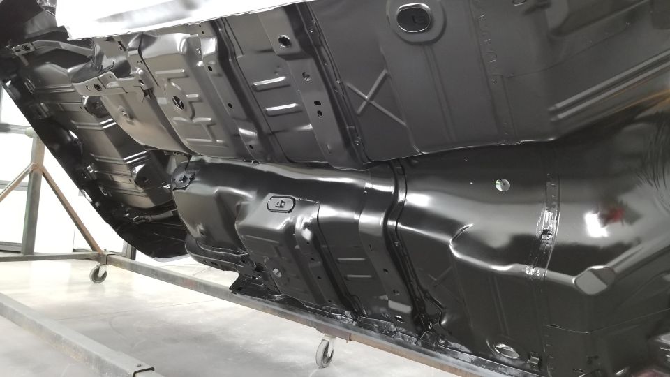 Black painted car undercarriage on a metal stand, viewed from below