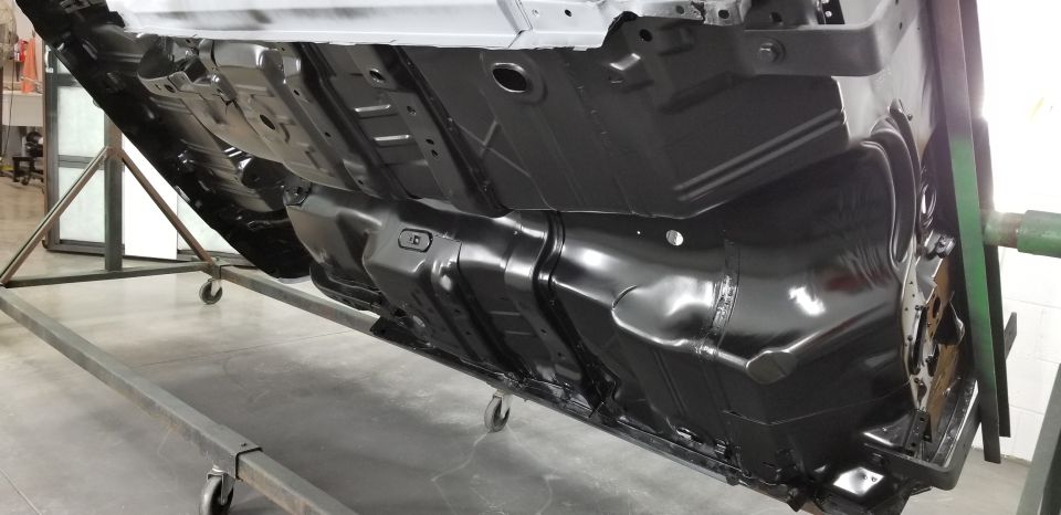 Underside of car chassis on lift, showing fuel tank and frame rails