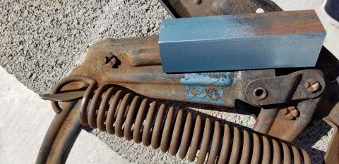 1970 Chevrolet Camaro - A close-up view of a rusty mechanical car part, possibly a spring assembly, with a small blue painted metal block resting on it.