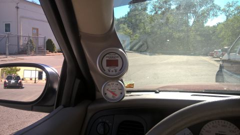 2004 Ford Crown Victoria - Aftermarket gauges are installed on the A-pillar, with a view of the road and a car in the side mirror.