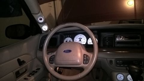 2004 Ford Crown Victoria - The dashboard of a car features a Ford steering wheel and illuminated gauges, with additional gauges mounted on the A-pillar.