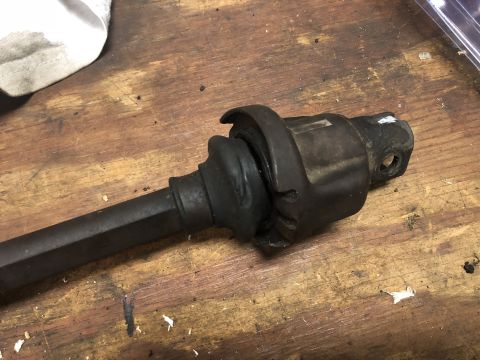 1980 Ford Bronco - Close-up view of a CV joint with a damaged rubber boot, resting on a wooden workbench.