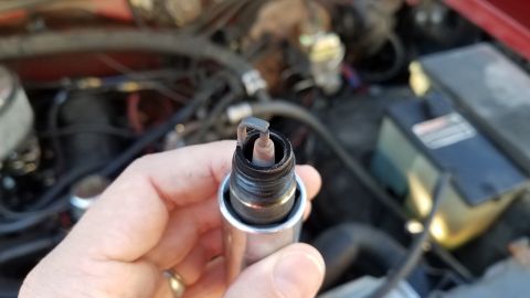 1985 Ford Bronco - A close-up of a spark plug with a bent electrode, held in a hand with the engine bay in the background.