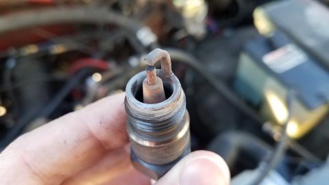 1985 Ford Bronco - A close-up view of a used spark plug being held, with the engine bay visible behind it.