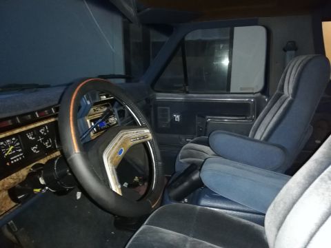 1996 Ford Bronco - The interior of a blue Ford truck shows velour seats and a wood-grain steering wheel, indicative of an older model.