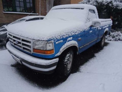 1994 Ford F-150 - A blue Ford F-150 truck is partially covered in snow, parked outdoors in winter.