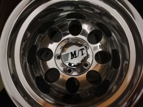 1996 Ford Bronco - A close-up view of a polished chrome wheel multiple circular openings and an M/T brand logo.