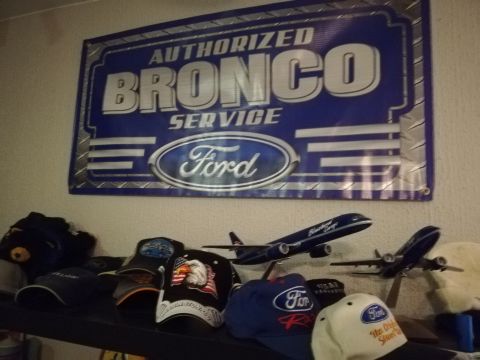 1996 Ford Bronco - A blue banner reading "AUTHORIZED BRONCO SERVICE" with a Ford logo is displayed above a shelf of hats and model airplanes.