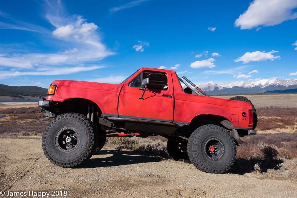 Red lifted SUV with large tires parked on a dirt road with mountains in the background