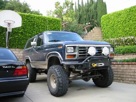 1985 Ford Bronco - Modified Ford Bronco parked in a driveway next to a black sedan.