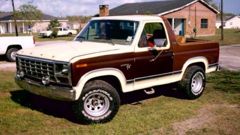 1980 Ford Bronco - This two-tone Ford Bronco is parked in a grassy area with a house and another truck in the background.