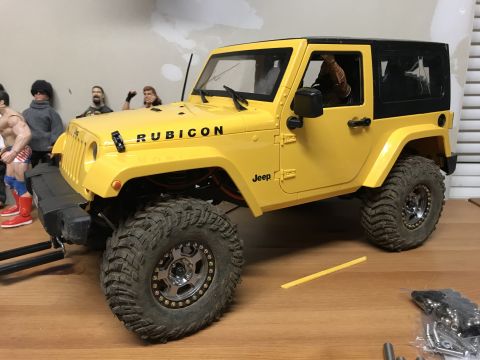 1989 Ford Bronco - A yellow toy Jeep Wrangler sits on a wooden surface, with several action figures in the background.